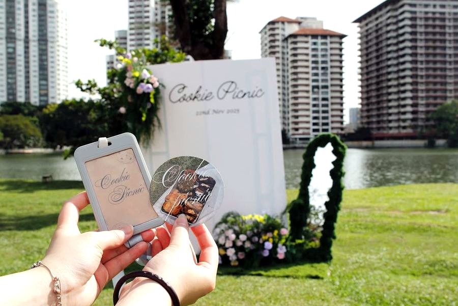 Holding a Cookie Picnic lanyard and sticker in front of the backdrop