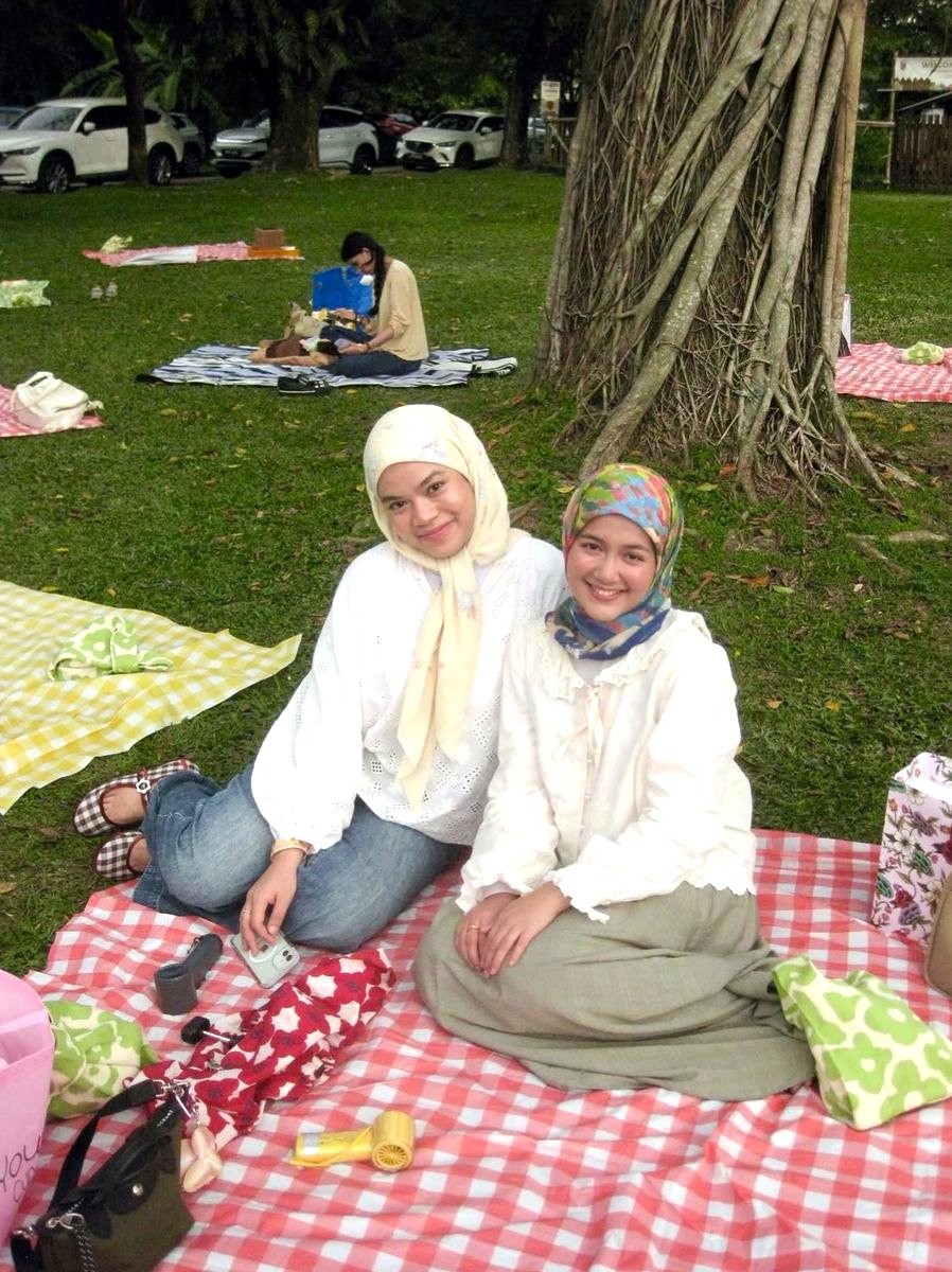 Two friends sitting on a gingham picnic mat under a tree