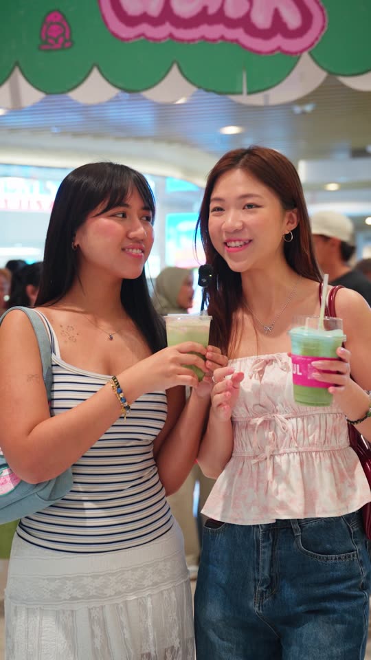 Two friends holding matcha drinks under the Matchawalk sign